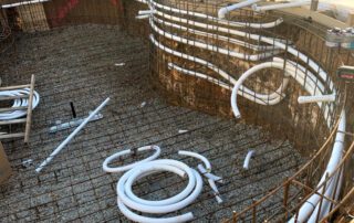 Pool construction site showing rebar framework and installed plumbing lines before concrete pour