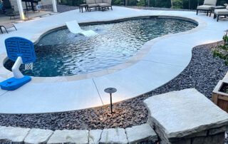 Completed inground pool with concrete decking, lounge seating, and backyard landscaping near a two-story home