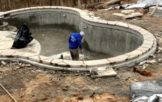 Worker applying finish inside a newly shaped inground pool during construction phase
