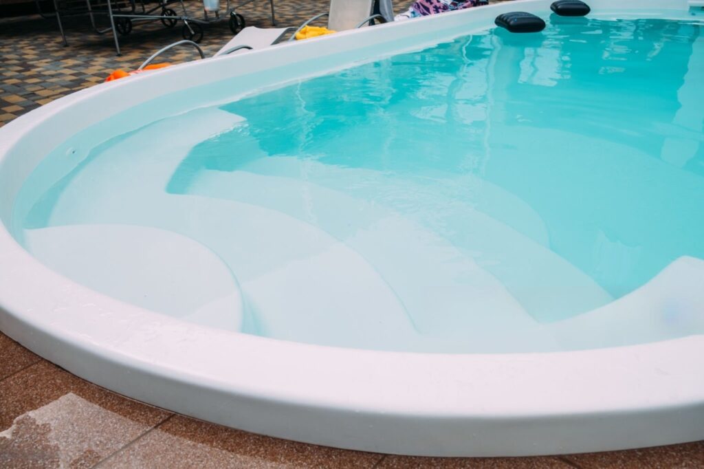 Fiberglass Pool With Built-In Steps Close-up of a white fiberglass swimming pool with clear blue water, built-in steps, rounded coping, and surrounding patio pavers.